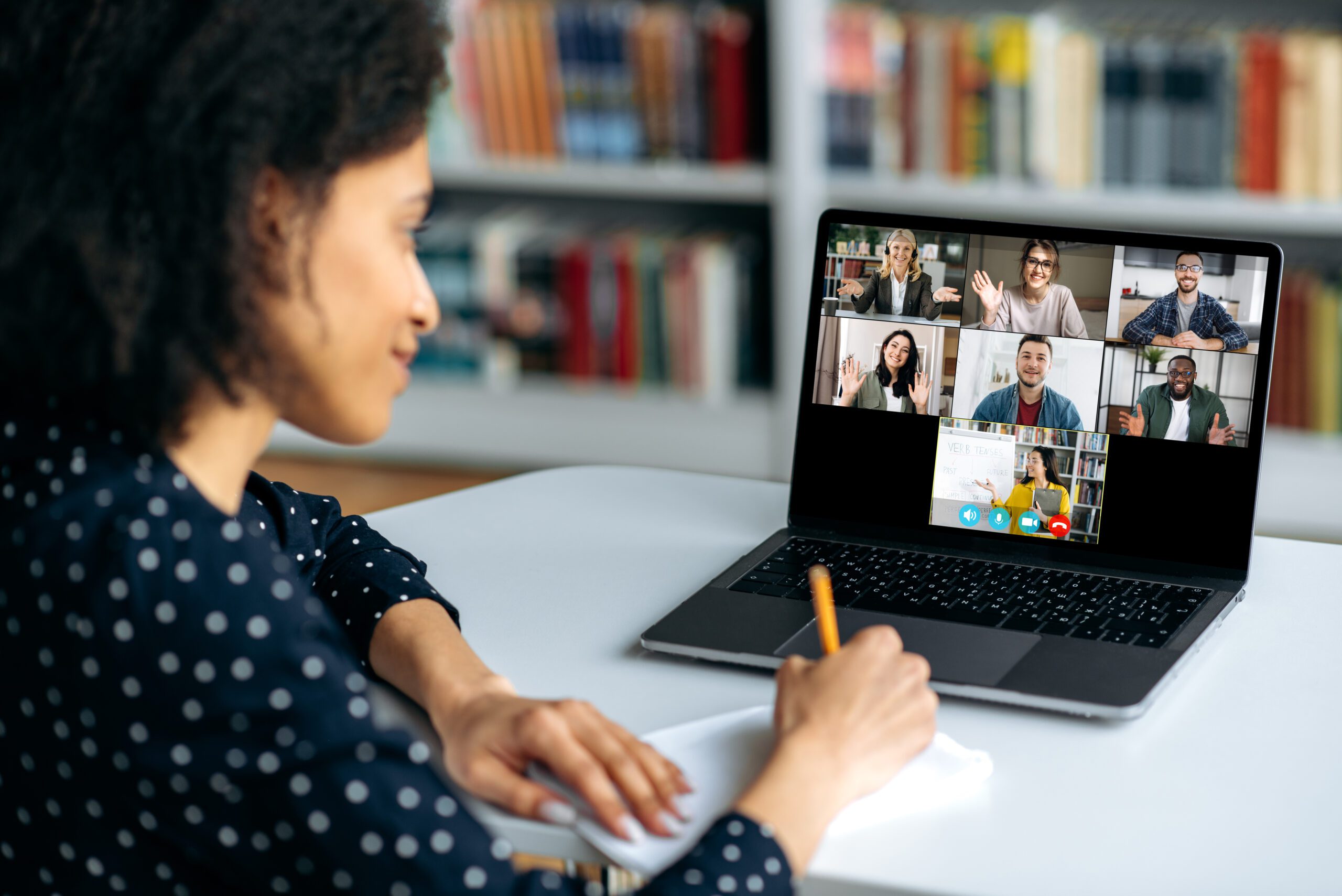 Teacher engaged in a video conference and taking notes.